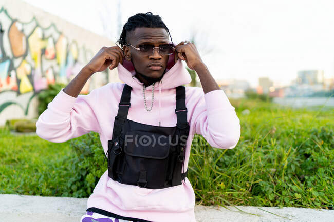 Confident African American male putting on hood sitting in stylish sunglasses and looking away — Stock Photo