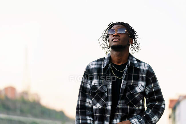 Low angle of confident young African American male in trendy sunglasses and casual outfit looking away — Stock Photo