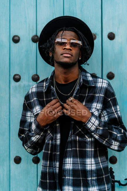African American male in trendy outfit and sunglasses standing and looking at camera near doorway — Stock Photo