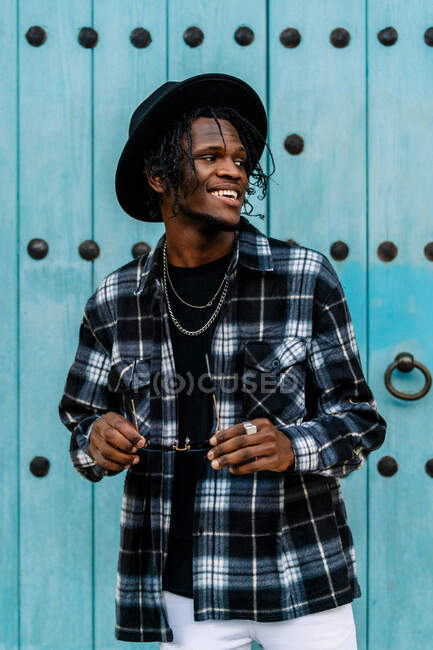 African American male in trendy outfit and sunglasses standing and looking away near doorway — Foto stock