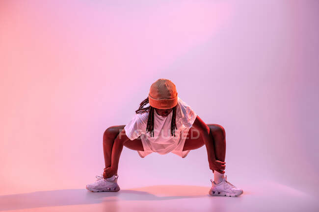 Full body of concentrated African American teen dancing with hands outstretched in studio with bright neon light — Stock Photo