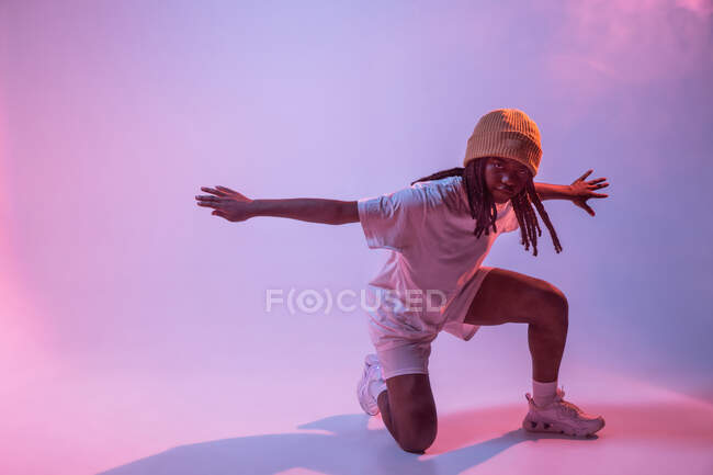 Все тело сконцентрированного афроамериканского подростка танцует с протянутыми в студии руками с ярким неоновым светом — стоковое фото