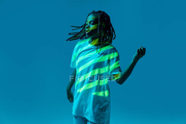 Динамічна афроамериканська дівчинка-підліток робить рух під час виконання міського танцю в неоновому світлі на синьому тлі — стокове фото