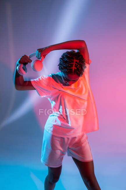 Serious African American teenage girl in headphones dancing in studio with bright glowing neon lights — Stock Photo