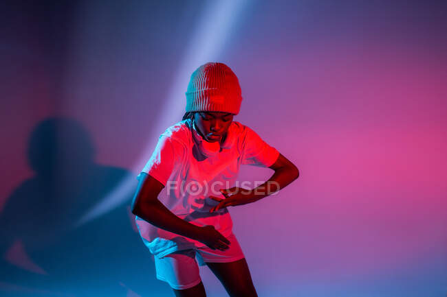 Grave menina adolescente afro-americana em fones de ouvido no pescoço dançando em estúdio com luzes brilhantes de néon — Fotografia de Stock