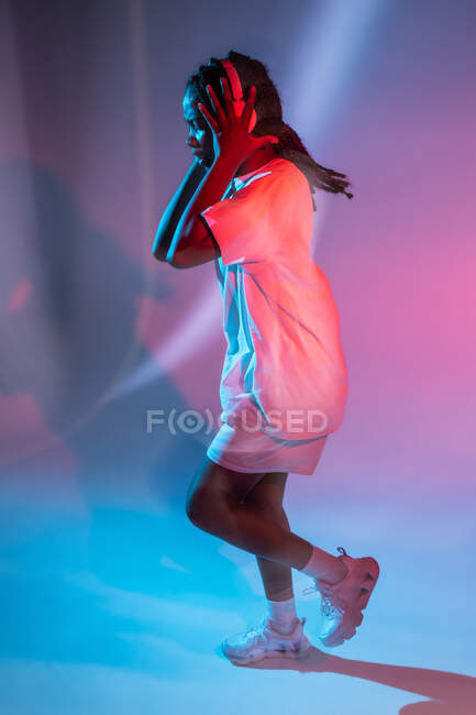 Afro americano adolescente godendo di musica in cuffie in neon studio — Foto stock
