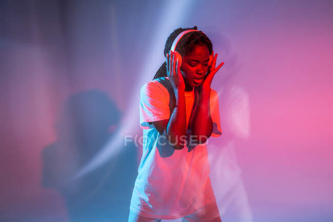 Afro americano adolescente con chiuso gli occhi godendo di musica in cuffie in neon studio — Foto stock