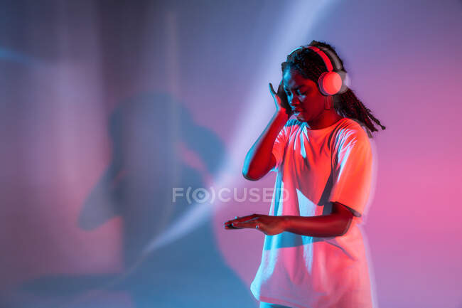 Афроамериканська дівчина - підліток із заплющеними очима насолоджується музикою в навушниках у неоновій студії. — стокове фото