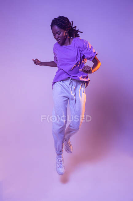 Full body of dynamic African American teen dancer leaping up while performing dance movement in bright studio — Stock Photo