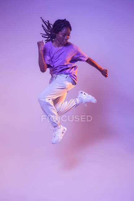 Corpo inteiro de dançarina adolescente afro-americana dinâmica pulando enquanto executa movimento de dança em estúdio brilhante — Fotografia de Stock