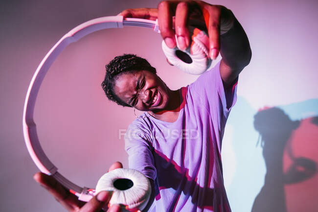 Menina adolescente louca com olhos fechados demonstrando fones de ouvido de pé em estúdio com cores brilhantes de néon — Fotografia de Stock
