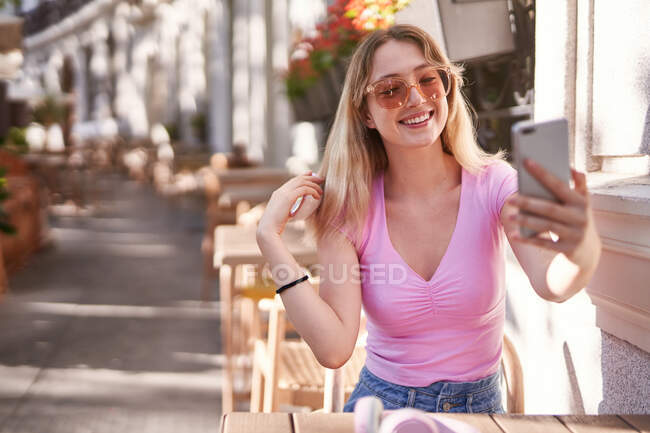 Веселая женщина делает селфи, сидя за столом в уличном кафе в Мадриде — стоковое фото