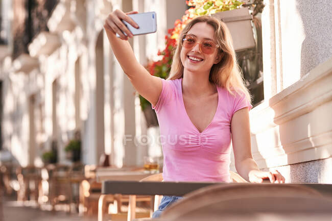 Cheerful woman taking selfie while sitting at table in street cafe in Madrid — Foto stock