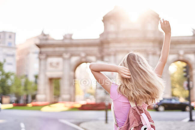 Back view female with hands raised standing in sunshine during trip in Madrid - foto de stock