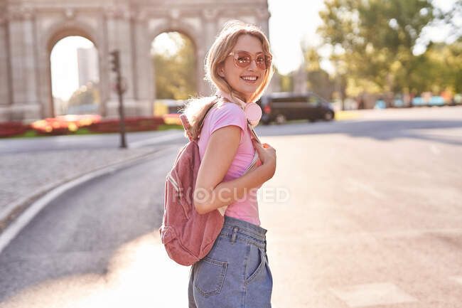 Mujer feliz de pie bajo el sol durante su viaje por Madrid y mirando a la cámara - foto de stock