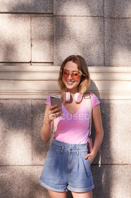 Cheerful woman browsing mobile phone while leaning on wall on street of Madrid — Stock Photo