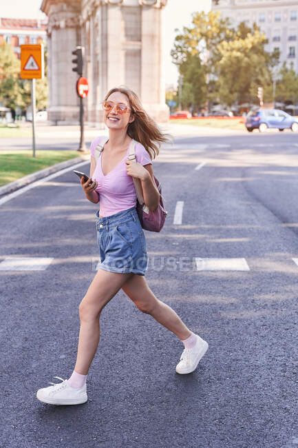 Seitenansicht einer jungen Frau, die auf einem Zebrastreifen geht und die Route per Handy in Madrid überprüft — Stockfoto