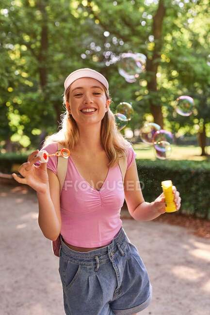 Беззаботная женщина дует пузыри, проводя солнечный день в зеленом парке Мадрида — стоковое фото