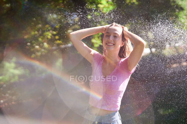 Cheerful female with hands on head standing in splashes in sunny park — Stock Photo