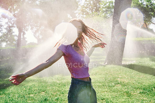 Веселая женщина стоит в брызгах в солнечном парке — стоковое фото