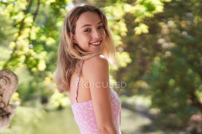 Femme souriante regardant la caméra portant une robe d'été dans un parc avec des arbres verts à Madrid — Photo de stock