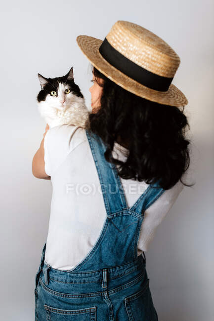 Back view of unrecognizable female horticulturist stroking and embracing fluffy cat at home - foto de stock