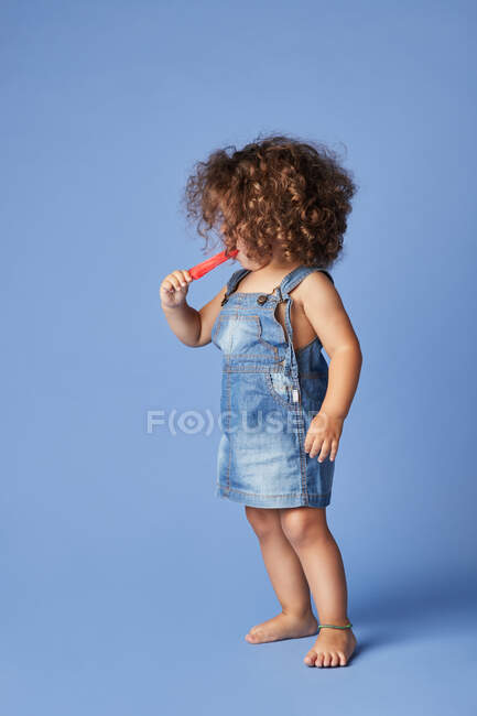 Неемоційна маленька дівчинка стоїть з таненням віскі на синьому фоні — стокове фото