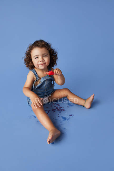 Corps complet d'adorable petite fille ravie assise en regardant la caméra avec de la glace fondue sur fond bleu — Photo de stock