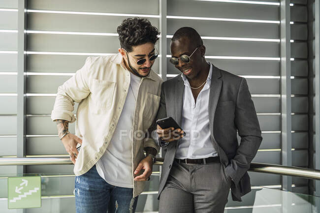 Cheerful multiracial friends looking a cellphone near ribbed wall — Stock Photo