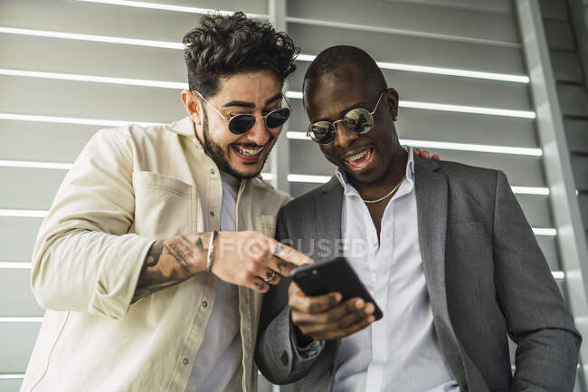 Alegre amigos multirraciais olhando um celular perto de parede com nervuras — Fotografia de Stock
