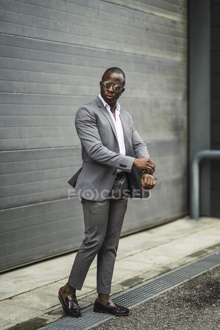 Чоловік чоловічої статі афроамериканського походження в офіційному костюмі і сонцезахисні окуляри переглядають час на вулиці — стокове фото