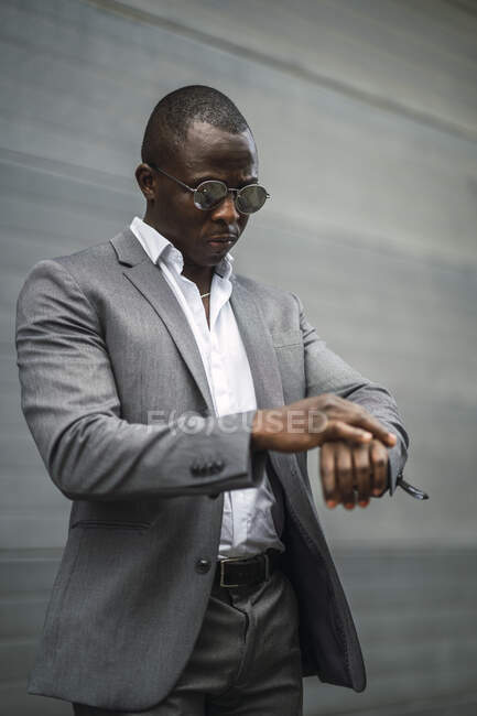 Masculin afro-américain exécutif masculin en costume formel et lunettes de soleil révisant le temps sur la rue — Photo de stock