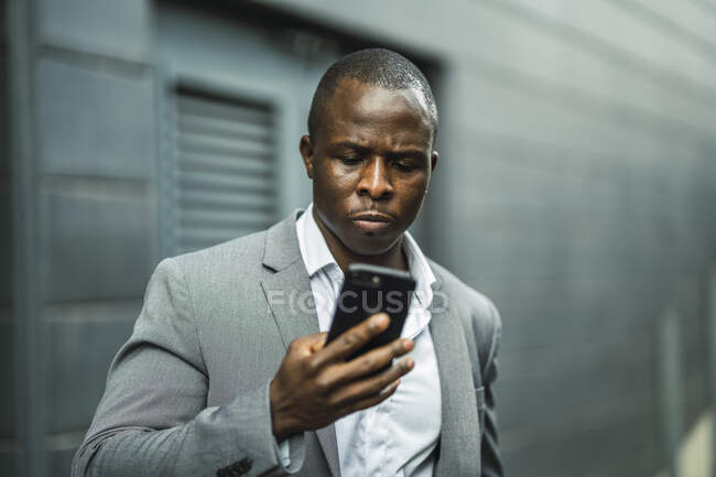 Серйозний чорний чоловічий бос, що переглядає мобільний телефон у місті — стокове фото