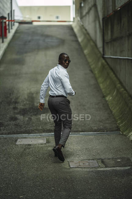 Back view of African American male entrepreneur in formal clothes and sunglasses with cellphone looking over shoulder in town — Stock Photo