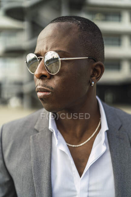 Empresario masculino afroamericano adulto en ropa formal y cadena con pendiente sobre fondo borroso a la luz del sol - foto de stock