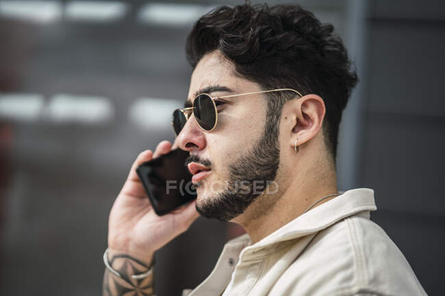 Focused bearded ethnic male in accessories and trendy apparel surfing internet on cellphone on street in daytime — Stock Photo
