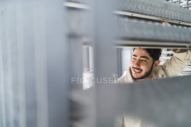 Through construction hole view of content young unshaven ethnic male looking away in city — Stock Photo