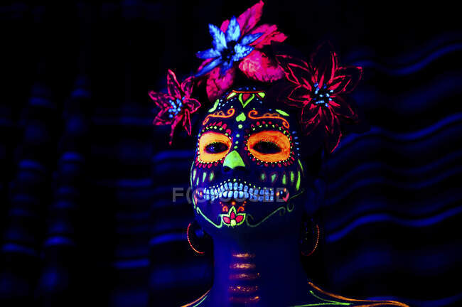 Femmina anonima in maschera multicolore con fiori in testa che guarda la macchina fotografica la notte di Halloween — Foto stock