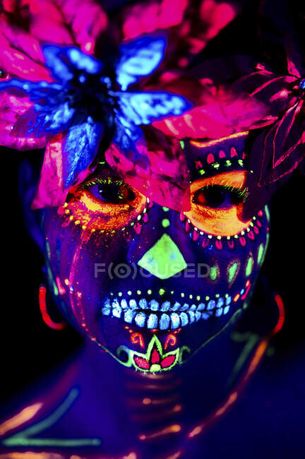 Anonymous female in multicolored masquerade mask with flowers on head looking at camera on Halloween night — Stock Photo