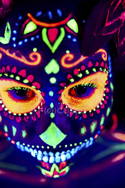 Femme anonyme en masque de mascarade multicolore avec des fleurs sur la tête regardant la caméra la nuit d'Halloween — Photo de stock