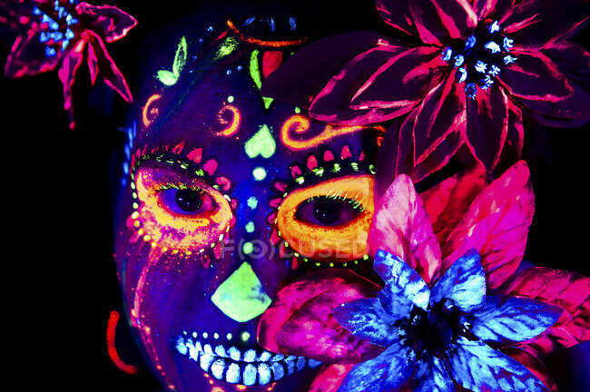 Mujer anónima en máscara de mascarada multicolor con flores en la cabeza mirando a la cámara en la noche de Halloween - foto de stock