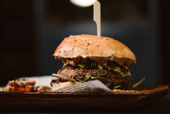 Low angle of yummy burger with vegetarian patty and grilled shiitakes between buns near sweet potato and carrot slices with alioli sauce on dark background — Stock Photo