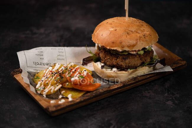 Leckerer Burger mit vegetarischem Patty und gegrillten Shiitakes zwischen Brötchen in der Nähe von Süßkartoffel- und Karottenscheiben mit Alioli-Sauce auf dunklem Hintergrund — Stockfoto