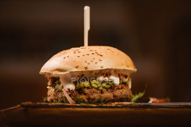 Low angle of yummy burger with vegetarian patty and grilled shiitakes between buns near sweet potato and carrot slices with alioli sauce on dark background — Stock Photo