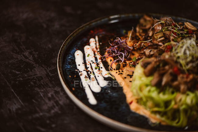 Вкусное веганское блюдо с цуккини-спагетти и ломтиками грибов с соусом, покрытыми красными ягодами и люцерной капустой на тёмном фоне — стоковое фото