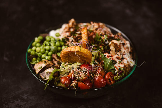 Tigela de saborosas fatias de batata-doce com tomates cereja perto de ervilhas verdes e sementes de gergelim no fundo escuro — Fotografia de Stock