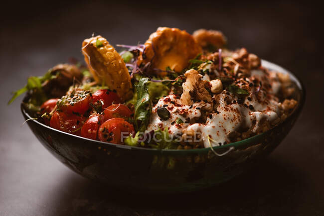 Ciotola di gustose fette di patate dolci con pomodorini vicino a piselli verdi e semi di sesamo su sfondo scuro — Foto stock