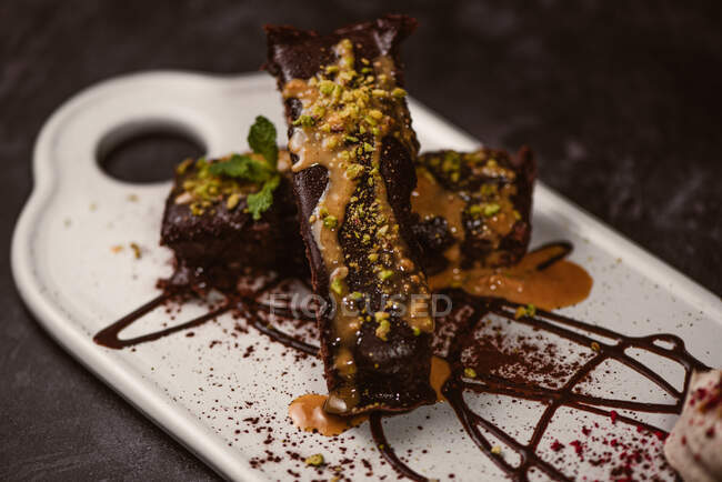 Tasty brownies covered with peanut butter and crunchy crushed pistachios near gelato scoop on plate with chocolate sauce — Stock Photo