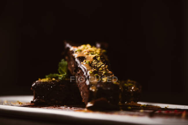 Tasty brownies covered with peanut butter and crunchy crushed pistachios near gelato scoop on plate with chocolate sauce — Stock Photo