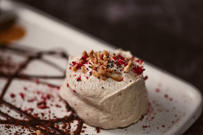 Paletta gelato al latte ricoperta di salsa di bacche dolci su piatto con condimenti in ristorante su fondo scuro — Foto stock